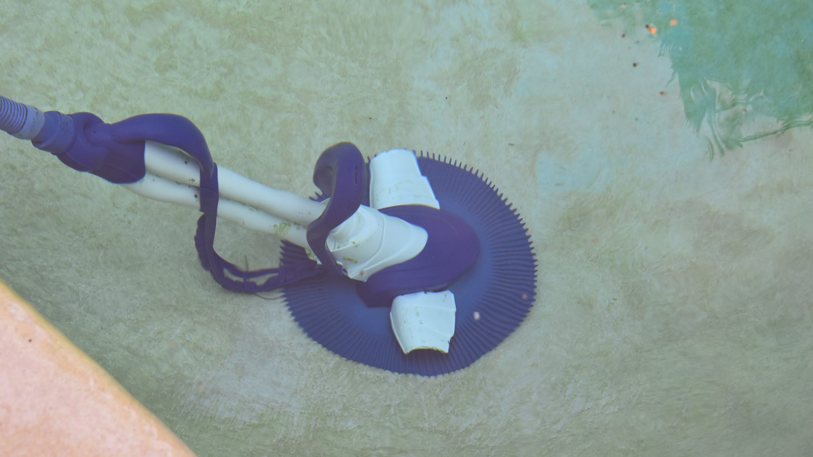 A diaphragm suction cleaner and its hose on the floor of a pool
